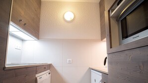 A compact kitchen with wooden cabinets, a built-in dishwasher, a washing machine, and a microwave.