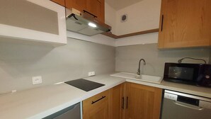 Una cocina compacta con armarios de madera, un microondas integrado y un lavavajillas.