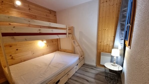 Habitación con literas, suelo de madera, una mesita con lámpara y un radiador.
