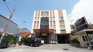 Hotel com entrada central, placa de identificação e área de estacionamento.