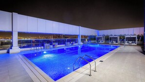 A rooftop swimming pool with clear blue water, surrounded by lounge chairs and a city view at night. - Courtyard by Marriott Al Barsha, Dubai (Dubai)