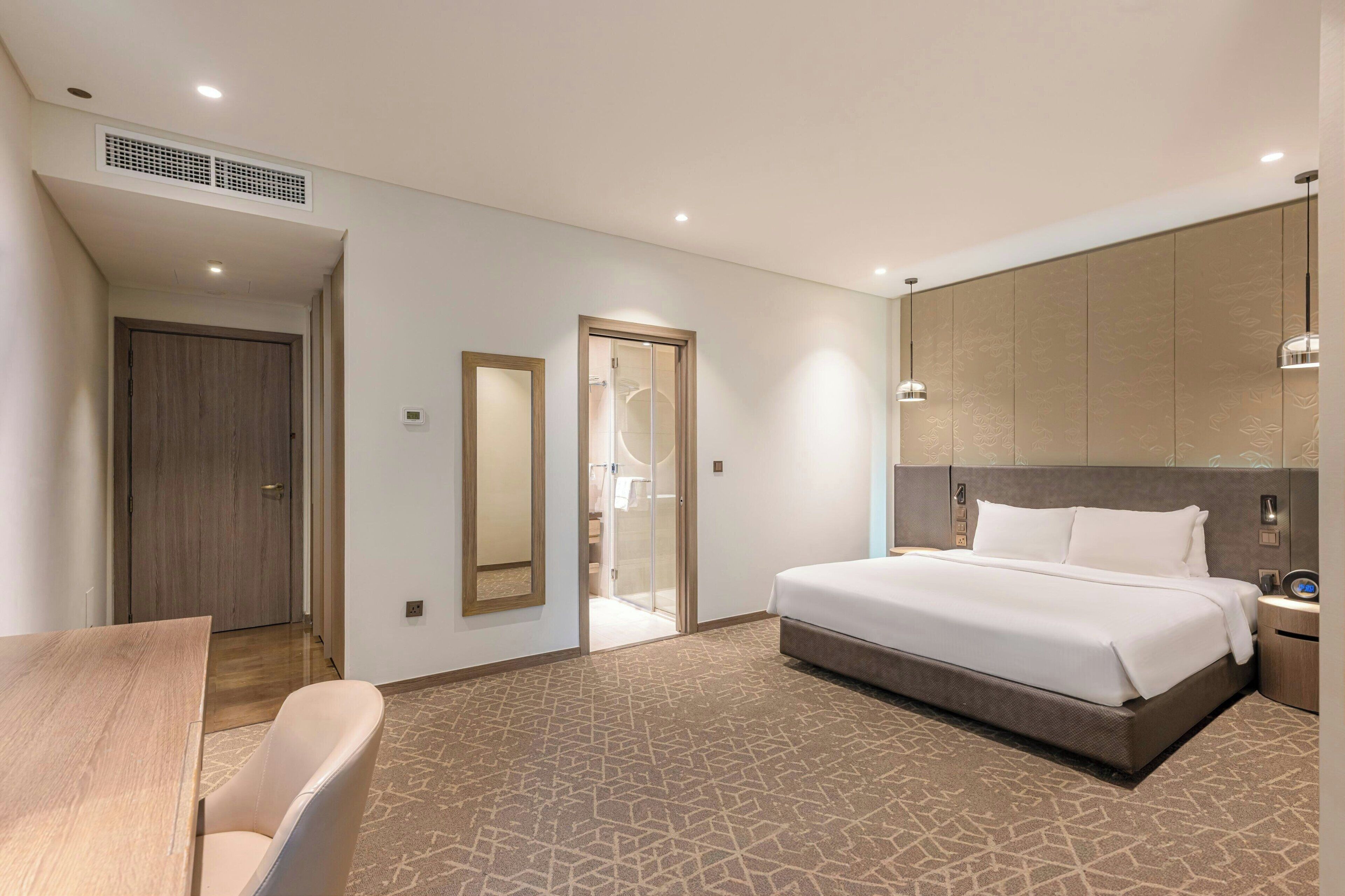 A modern hotel room with a large bed, a wooden desk, and a mirror.