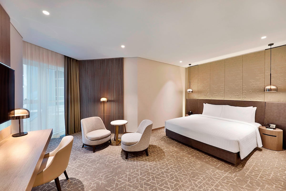 A hotel room with a bed, two armchairs, a desk, and a TV.