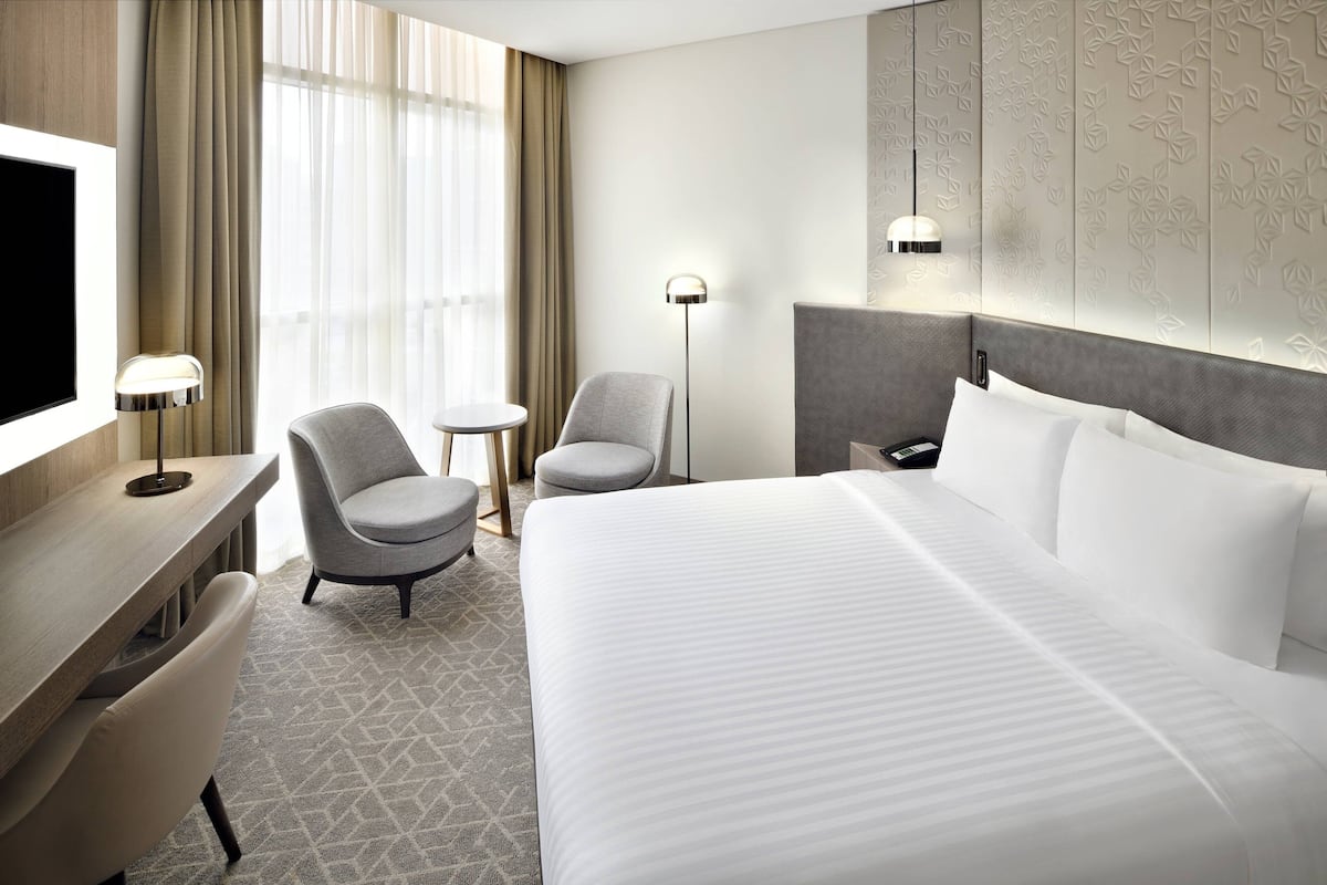 A hotel room with a large bed, a desk with a chair, a small round table, and a TV.