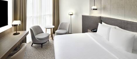 A hotel room with a large bed, a desk with a chair, a small round table, and a TV.