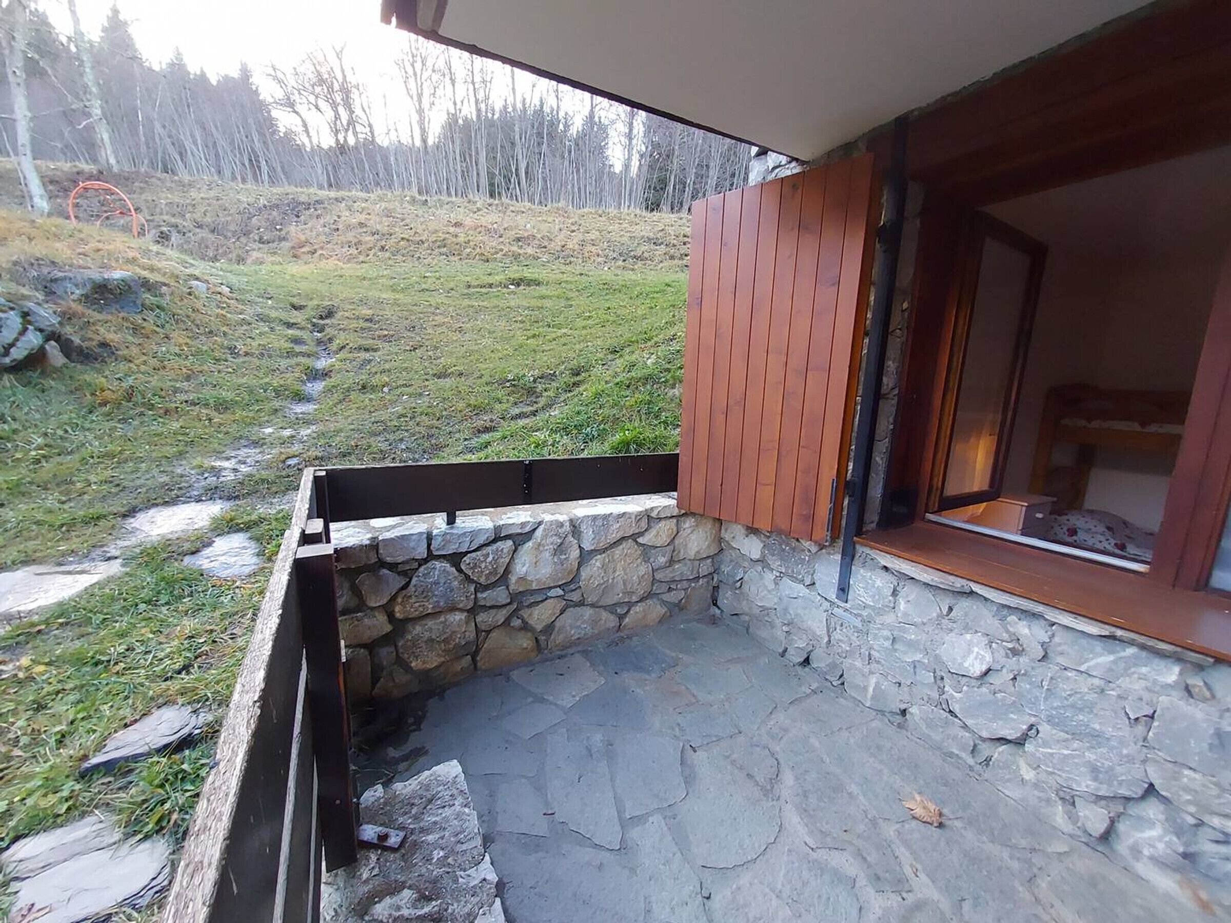 A stone exterior with a wooden window frame, a stone wall, and a grassy area with a path.