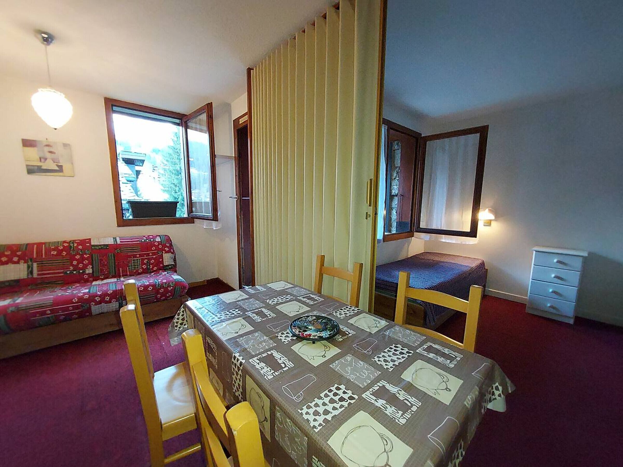 A small, cozy room with a dining table, two chairs, a sofa, and a bed.
