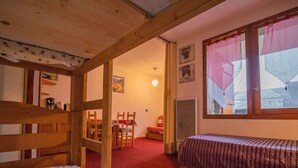 A cozy room with a wooden bunk bed, a single bed, a red carpet, a dining area with chairs, and a large window with curtains. - Quiet apartment in Valmorel, pets allowed, 5 people (Valmorel)