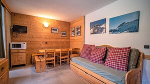 Ein gemütliches Blockhäuschen-Interieur mit einem Holztisch, Bänken, einer Couch mit karierten Kissen, einem an der Wand befestigten Fernseher und gerahmten Bildern.