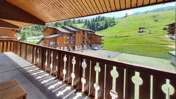 Ein Holzbalkon mit Blick auf ein Chalet und eine grüne Hügelkuppe.