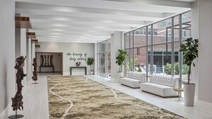 A spacious hallway with a patterned carpet, a white sofa, and large windows offering a view of a brick building. - Residence Inn by Marriott Greenville Downtown (Greenville)