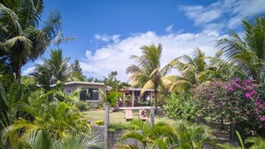Un jardin tropical avec une maison, des palmiers et un hamac.