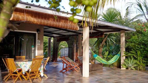 Une terrasse couverte avec des chaises et des tables en bois, un hamac et une végétation tropicale luxuriante.