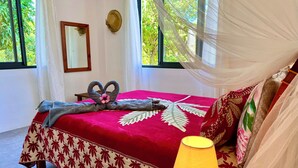 Un lit avec une couvre-lit rouge et blanche à motifs de feuilles, une serviette décorative et un baldaquin.
