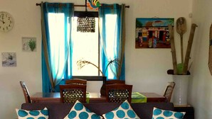 Un salon avec un canapé, des coussins à motifs, une table basse sur laquelle se trouve un livre, et une horloge murale.