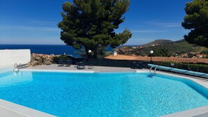 Una piscina cristallina con bordo piastrellato, circondata da alberi e affacciata su una cittadina costiera.