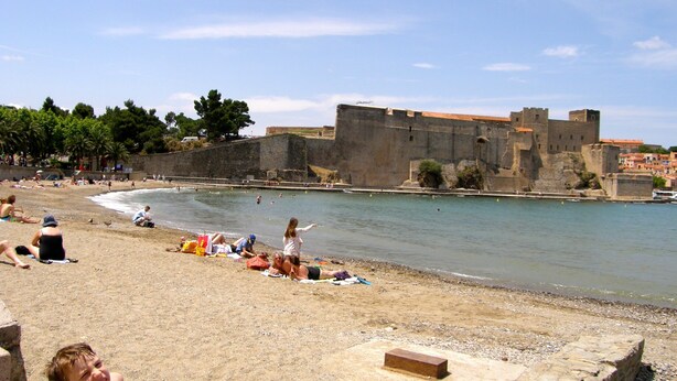 Una spiaggia con un muro di pietra e un castello sullo sfondo.