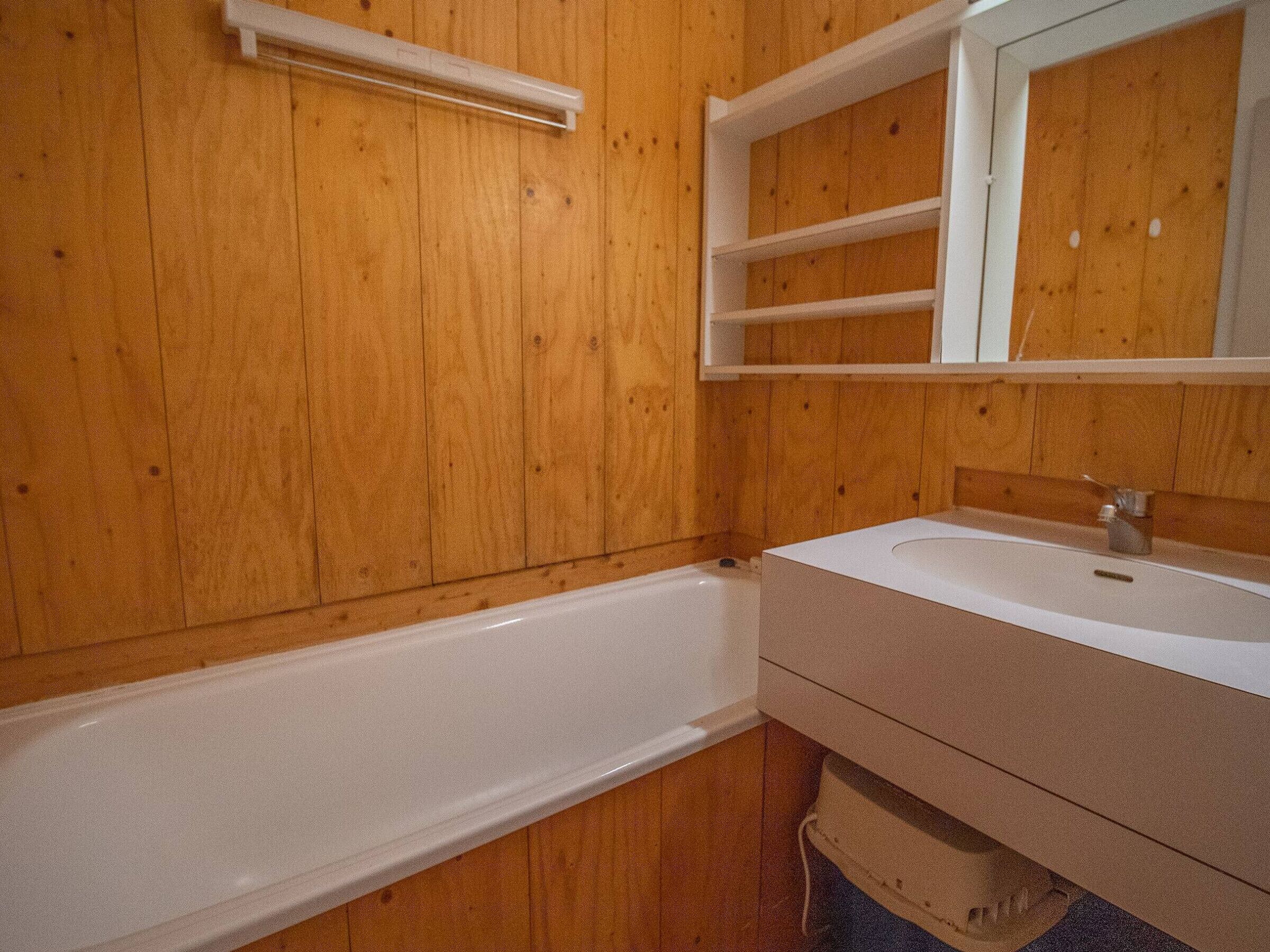 Een badkamer met houten wanden, een witte badkuip en een wastafel met spiegel.