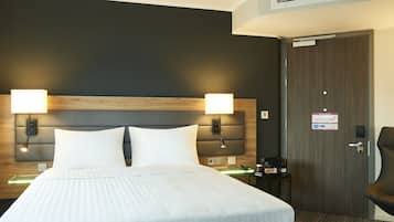 A hotel room with a large bed, two bedside lamps, a nightstand with a coffee maker, and a door with a sign.