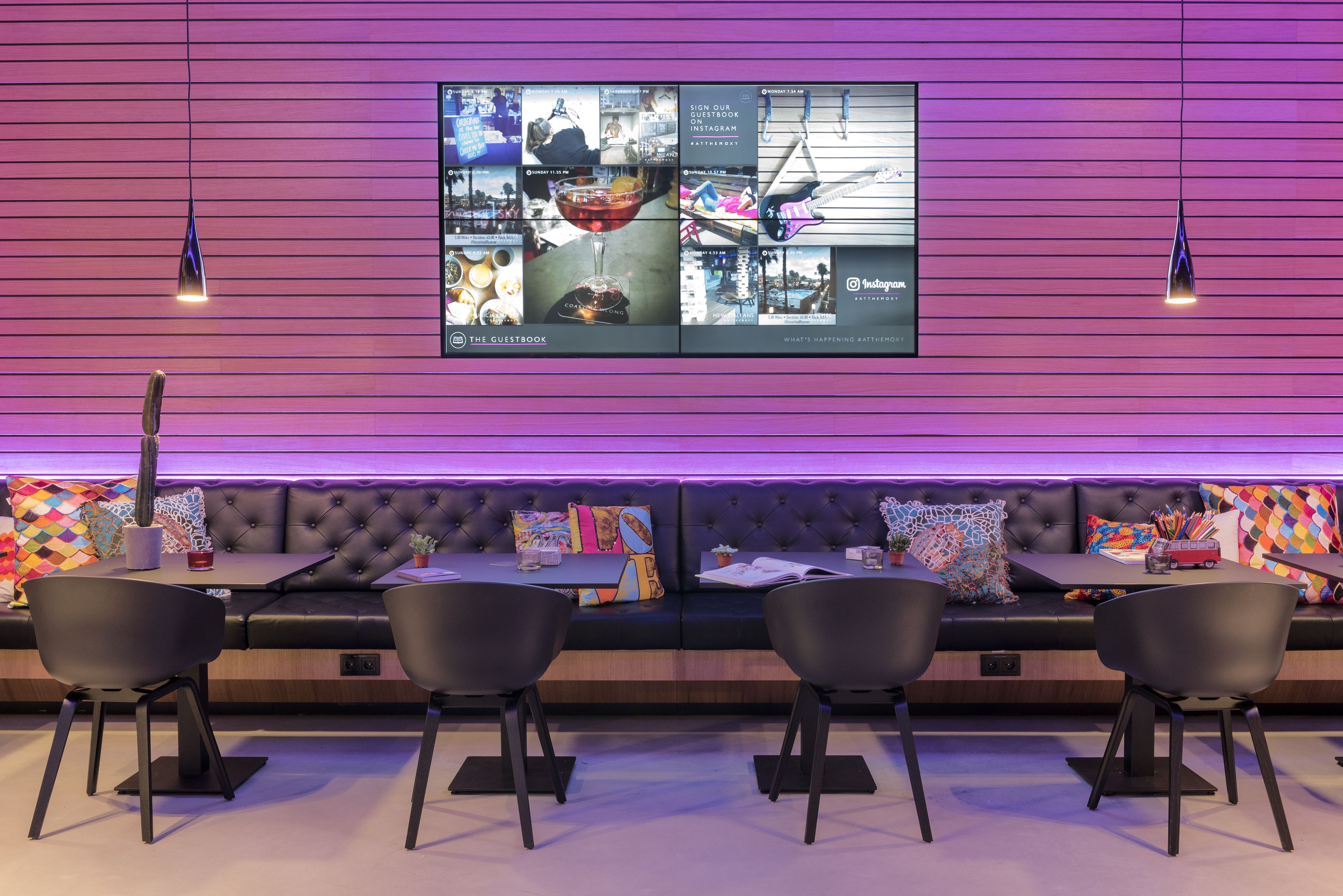 A modern interior with a large digital display, a black leather sofa, and black chairs.
