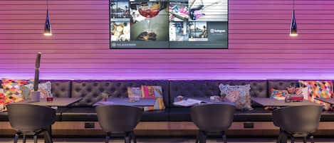 A modern interior with a large digital display, a black leather sofa, and black chairs.