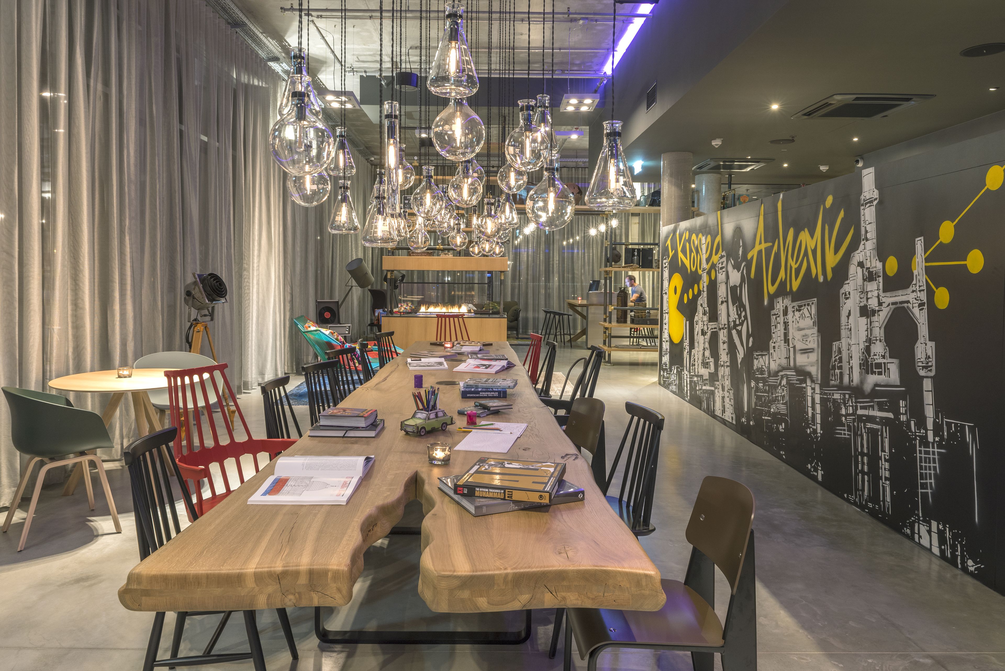 A long wooden table with chairs, hanging glass light fixtures, and a mural on the wall.