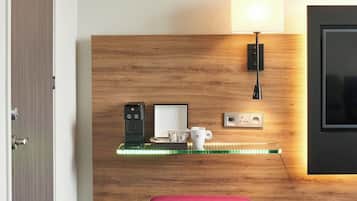 Habitación de hotel con cabecera de madera, mesita de noche con lámpara, reposapiés rojo y televisor en la pared.