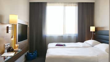 Una habitación de hotel con una cama, un escritorio con lámpara, un televisor y una ventana con cortinas.