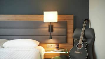 Una cama bien tendida con sábanas blancas, una lámpara de noche, una guitarra y una mesita con una taza y un libro.