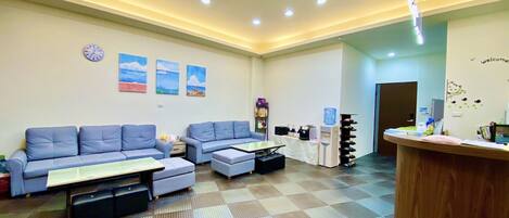 Un hall de hotel con piso a cuadros, sofás azules, mostrador de recepción, dispensador de agua y arte en las paredes.