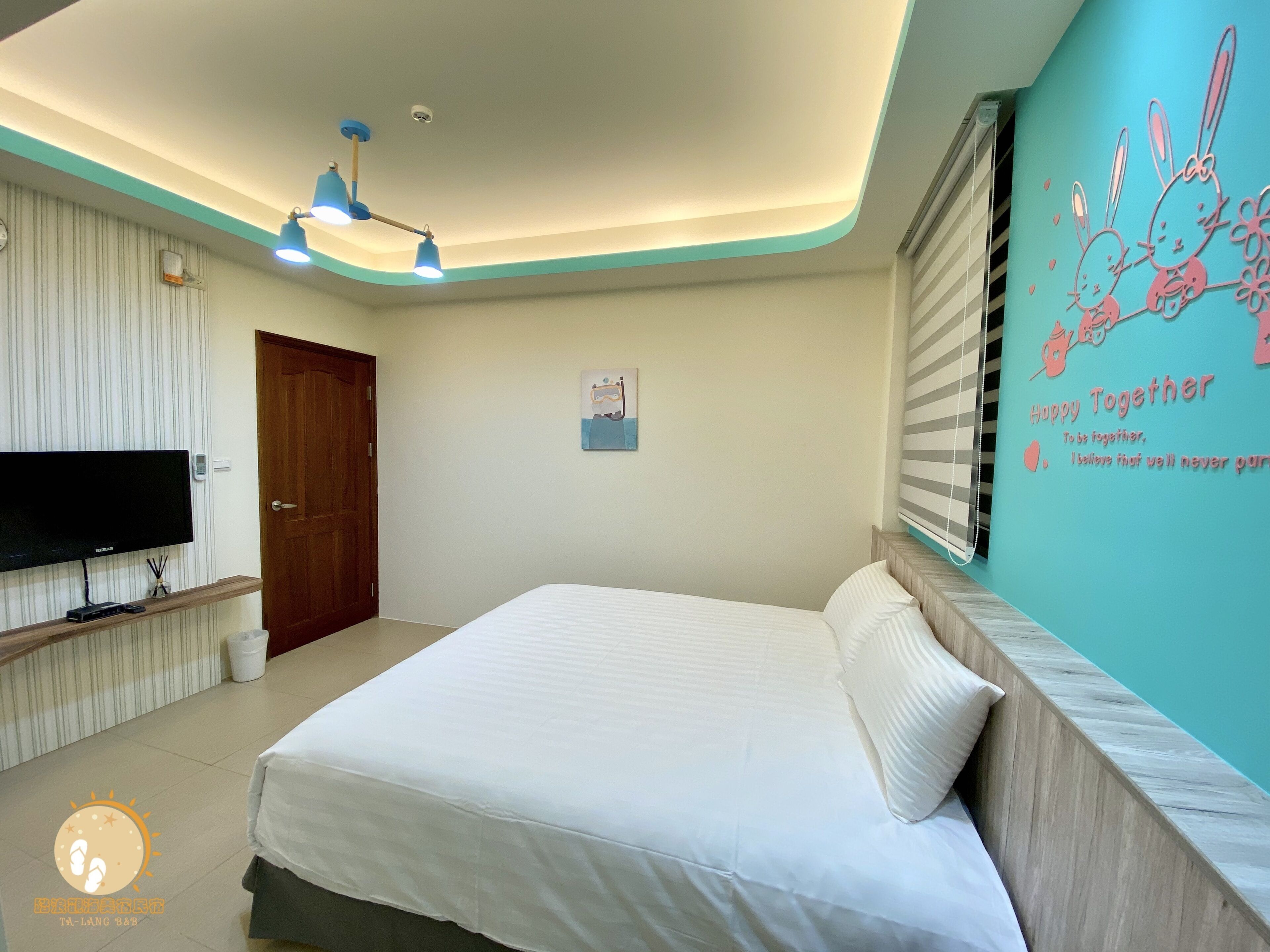 Un dormitorio con cama, televisión, lámpara en el techo y decoración en la pared.