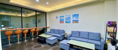 A modern living room with a blue sofa, two ottomans, a coffee table, and a glass partition.
