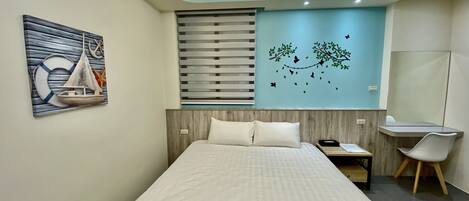 A modern hotel room with a large bed, a desk, and a chair. There is a wall decoration of a sailboat and a tree with butterflies.