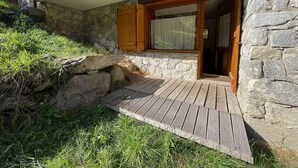Ein Steinhaus mit einer Holzterrasse, die zu einer Glastür führt.