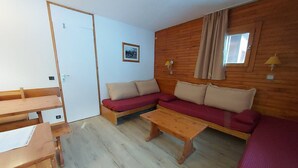Un espacio habitable pequeño con piso de madera, un conjunto de sofás, una mesa de madera y una puerta.