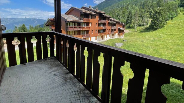 Un balcón de madera con vistas a una cabaña de montaña con varios balcones y un paisaje verde y exuberante.