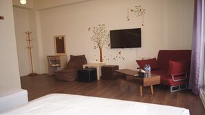 A modern hotel room with a bed, a red armchair, a wooden coffee table, a TV mounted on the wall, and a coat rack. - Shimmer B&B (Magong)