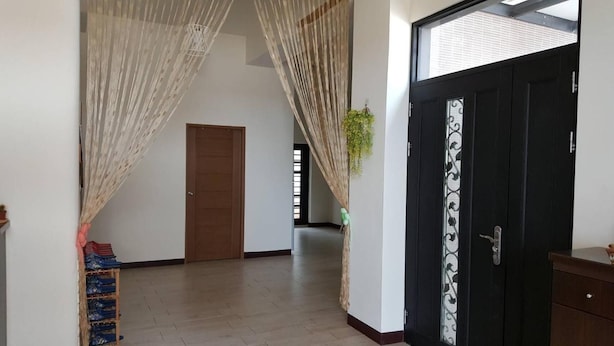 A hallway with a wooden door, a black door with decorative glass, and a plant. - Shimmer B&B (Magong)