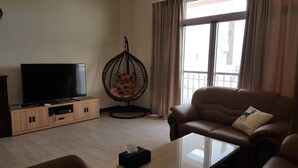 A living room with a leather sofa, a TV on a wooden cabinet, a hanging chair, and a large window with curtains. - Shimmer B&B (Magong)
