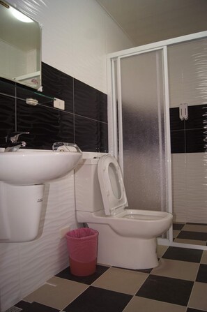 A bathroom with a white sink, toilet, and a glass shower enclosure. - Shimmer B&B (Magong)