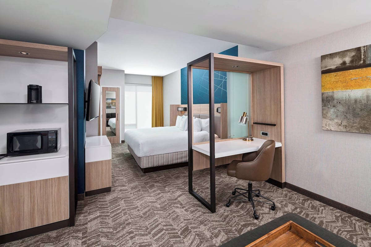 Habitación de hotel con cama, escritorio, silla, microondas y televisión.