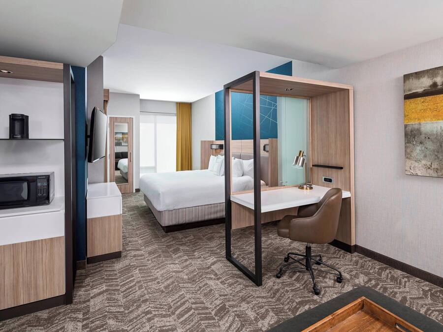 Ein Hotelzimmer mit Bett, Schreibtisch, Stuhl, Mikrowelle und Fernseher.