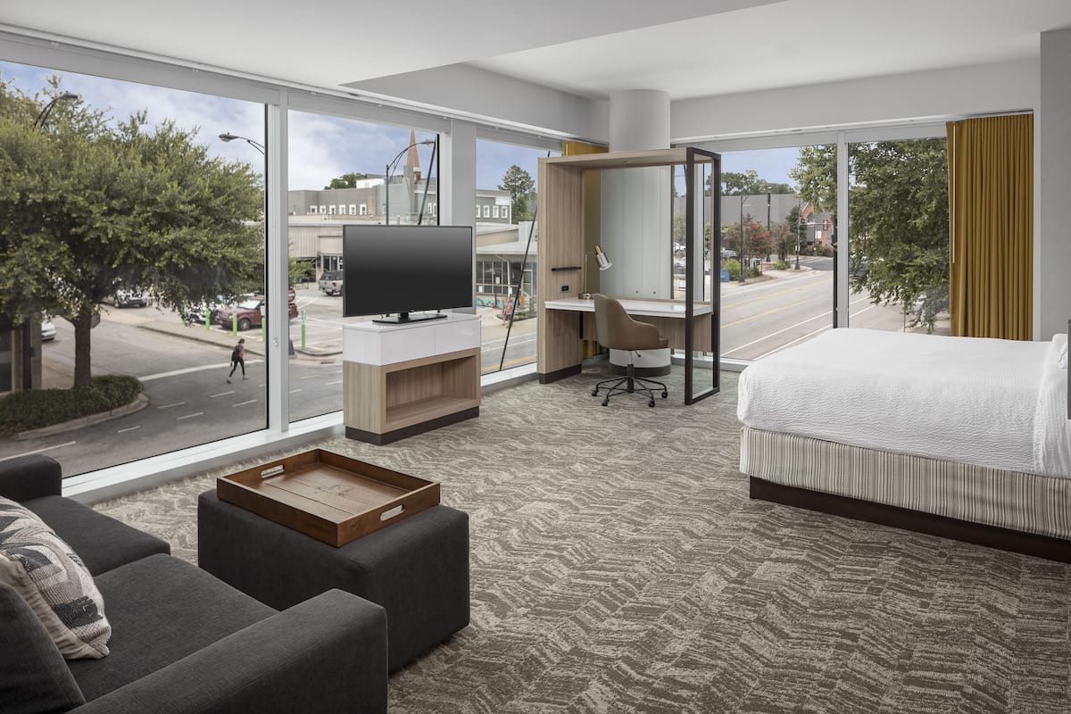 Una habitación de hotel moderna con un ventanal grande, una cama, un escritorio y una televisión.
