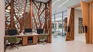 Un espacio de oficina moderno con un separador de madera, dos escritorios con computadoras, sillas verdes y una puerta de vidrio que da al exterior.