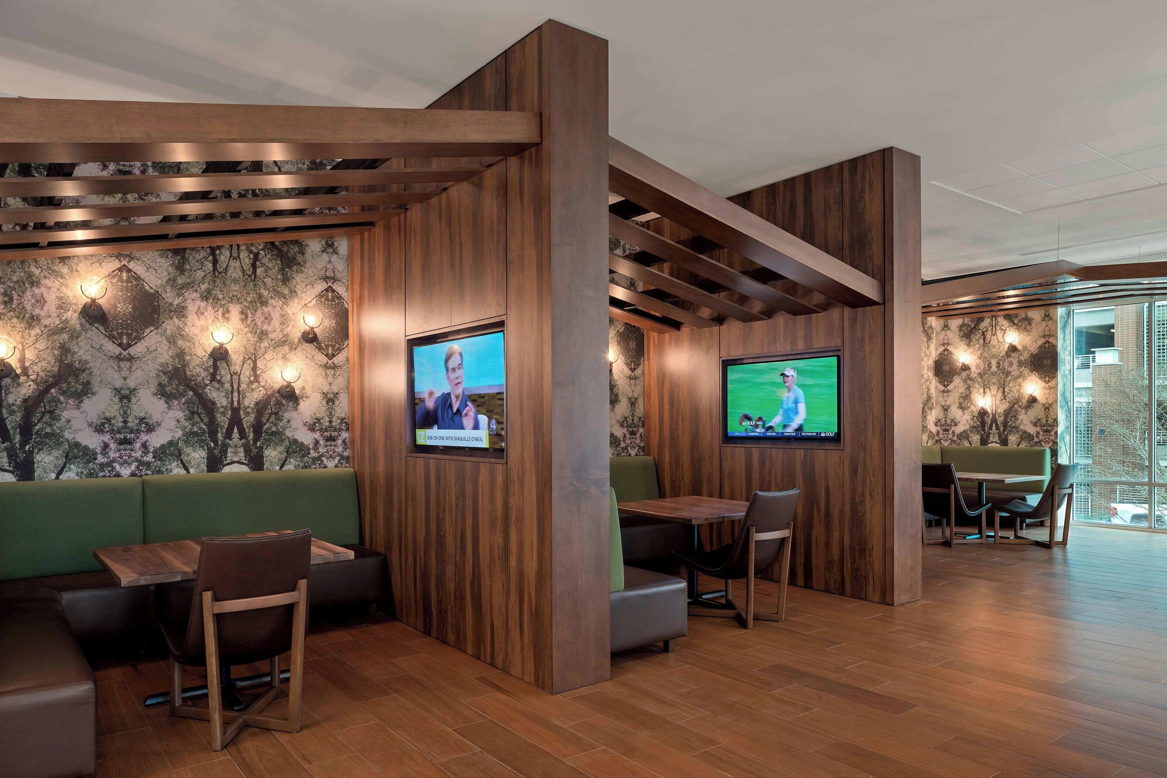 Un espace de détente moderne avec des panneaux de bois, des sièges verts et deux téléviseurs à écran plat fixés aux murs.