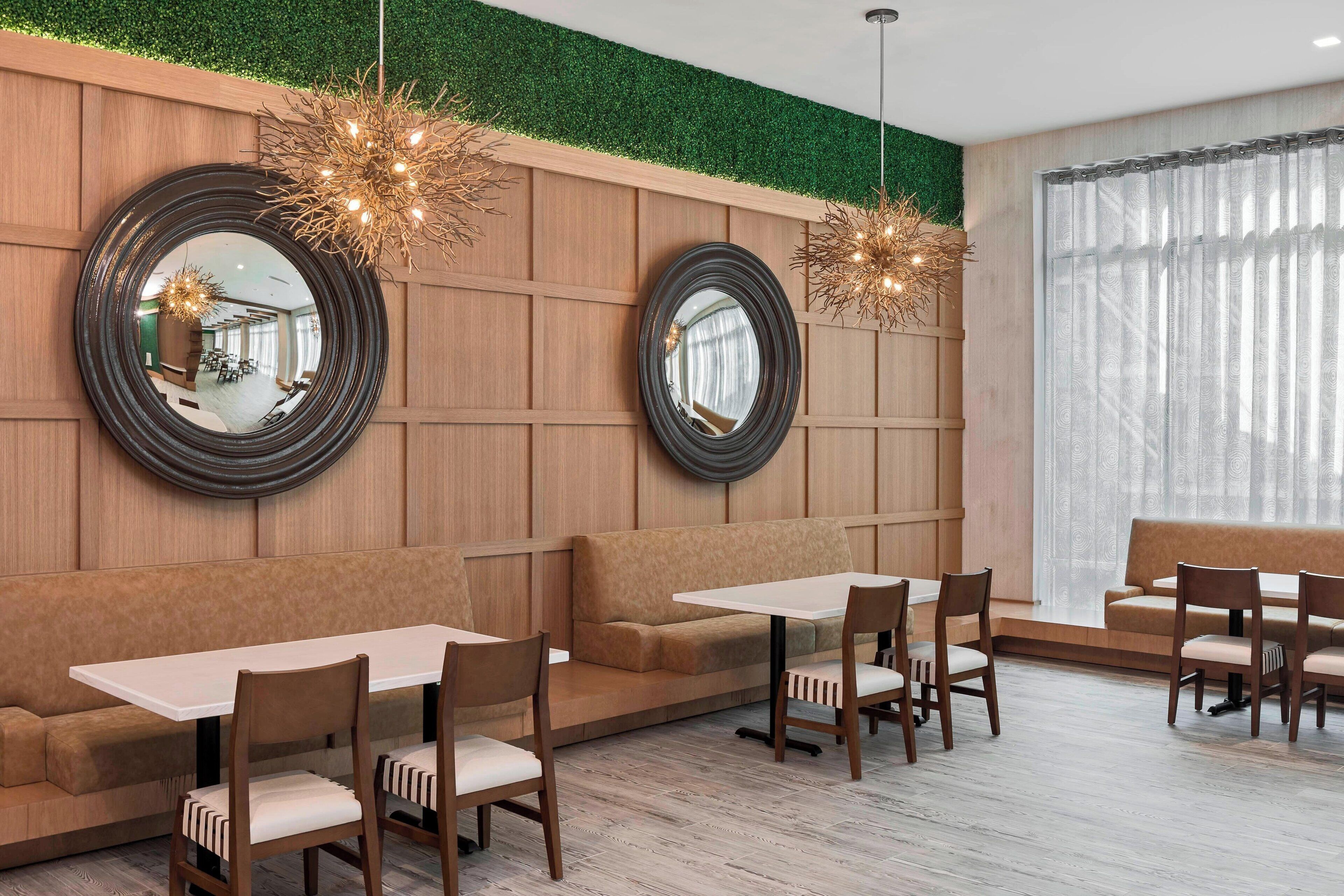 A modern restaurant interior with wooden panel walls, round mirrors, and a green artificial grass ceiling.