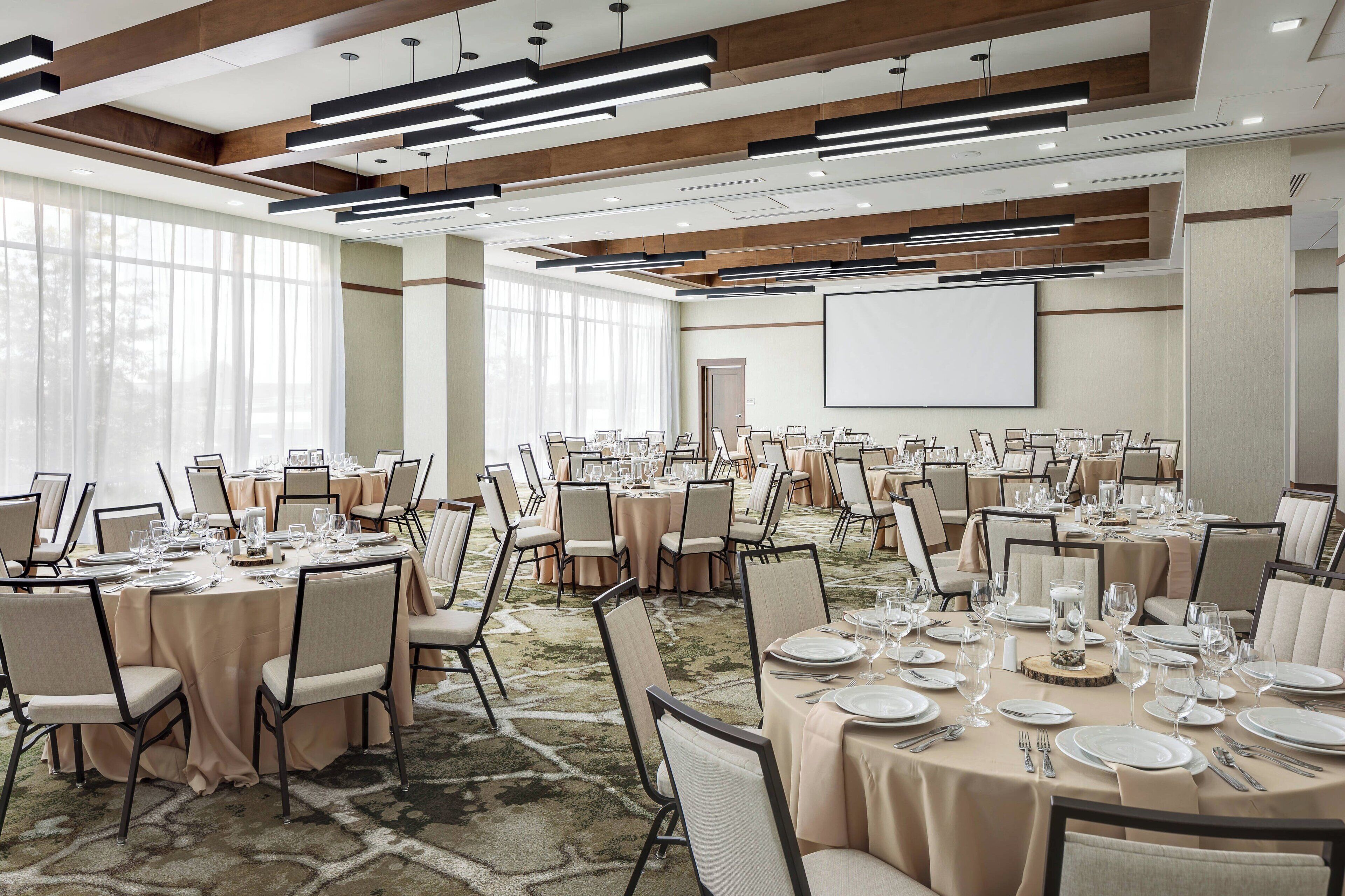 A large conference room with multiple round tables set for dining, equipped with chairs, plates, glasses, and cutlery.