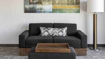 A modern living room with a dark grey sofa, a patterned throw pillow, a wooden tray, and a tall floor lamp.