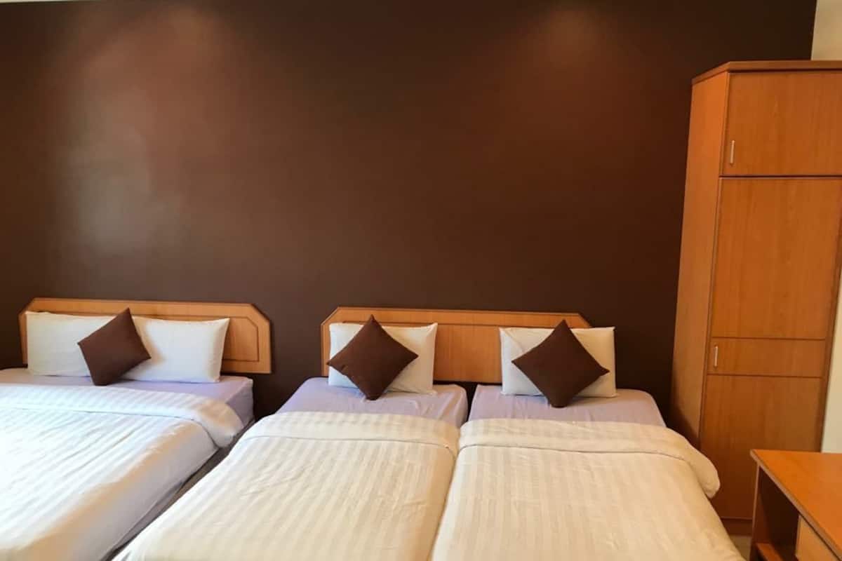Habitación de hotel con tres camas individuales, cada una con cabecero de madera y ropa de cama blanca. Se observa un armario de madera a la derecha.