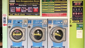 Una lavandería pública con tres lavadoras de 16 kilogramos, instrucciones y un tablón de información para clientes.